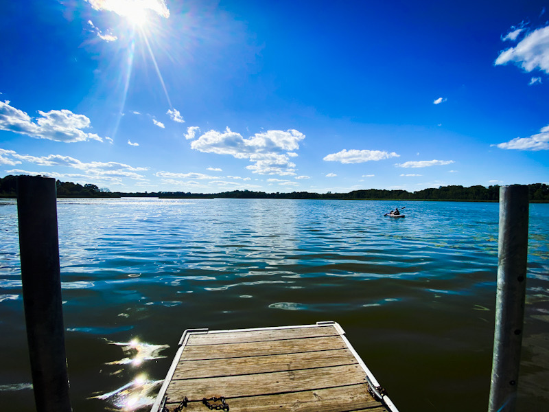 Fishing pier on a blue lake with kayaker in distance